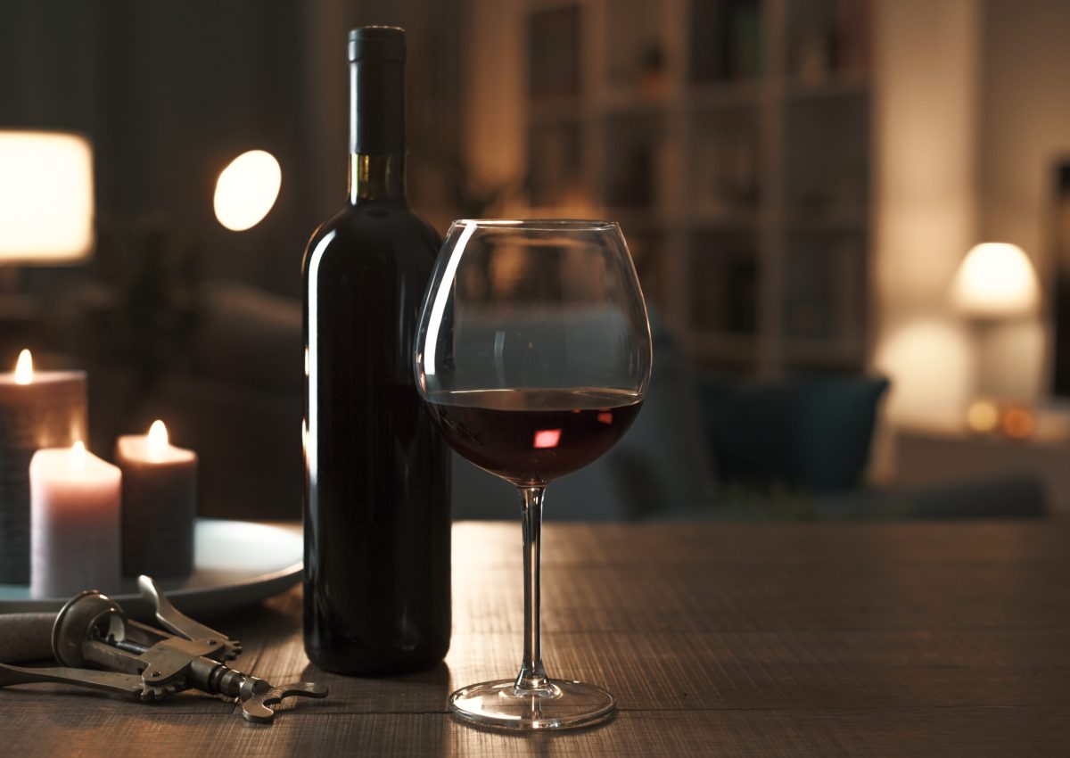 Red wine tasting at home: wine bottle, wineglass, corkscrew and candles on a table in the living room at night